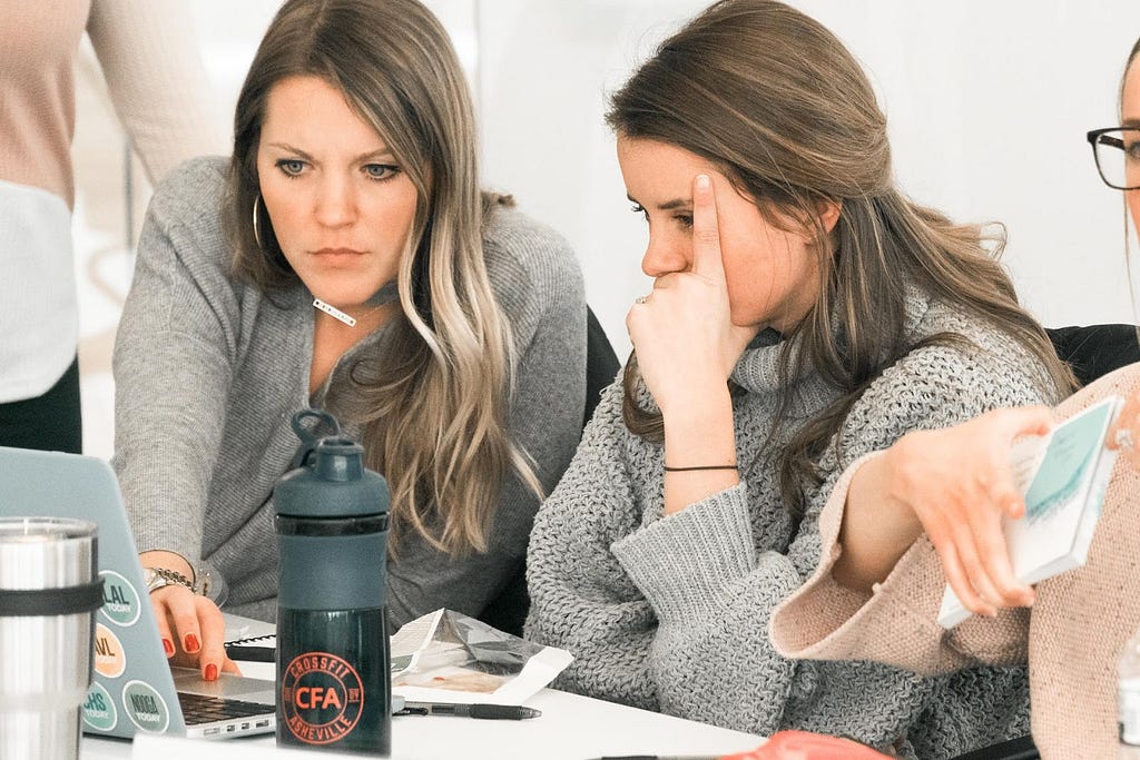 Two women work together on a computer.