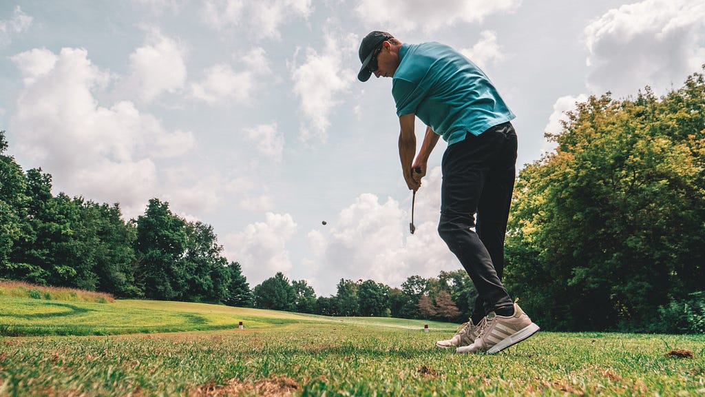 A man hitting his 5 iron into a beautifully green fairway.