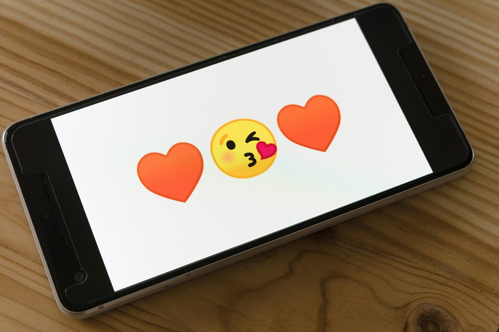 Phone screen showing emojis: heart, kissing face, heart.