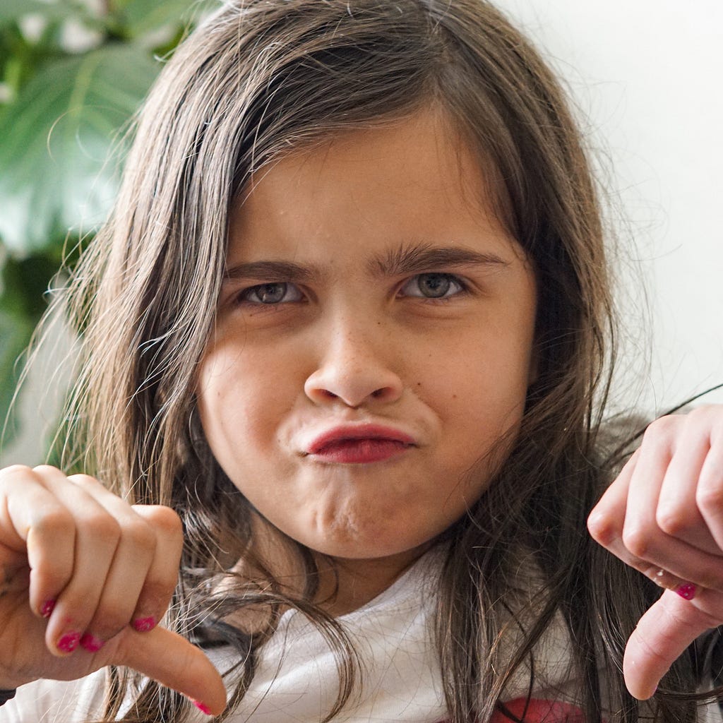 A young girl frowning and giving two thumbs down