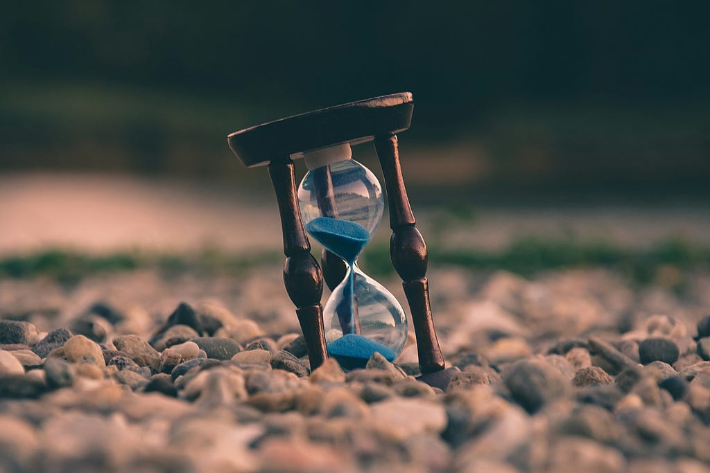 An hourglass with blue sands, sitting on a bed of rocks.