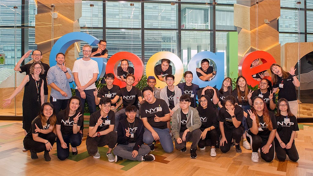 Group photo of students and workshop moderators posing in front of a large Google logo.