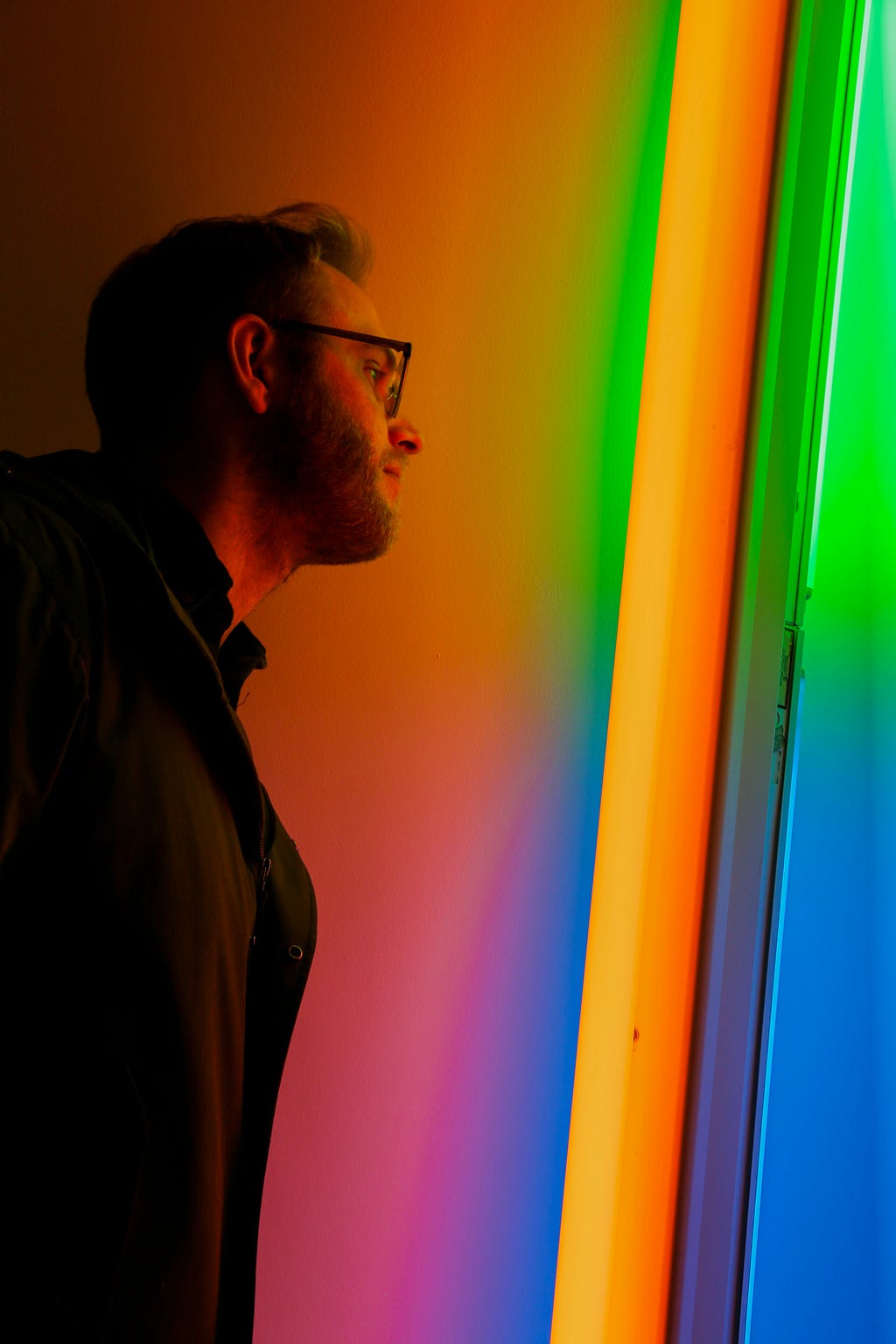 A man looks through a doorway illuminated with colorful gradients