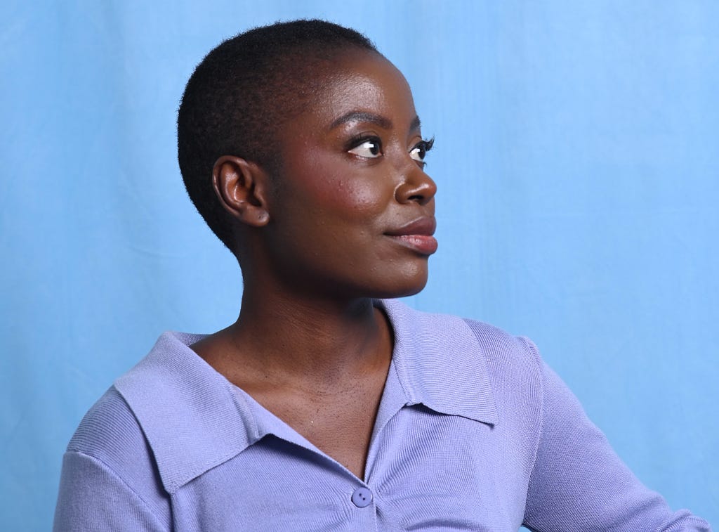 Portrait photo of Wabala Studio founder Anne-Marie Mulumba on a blue background. She is wearing a lavander shirt and looking away to the right