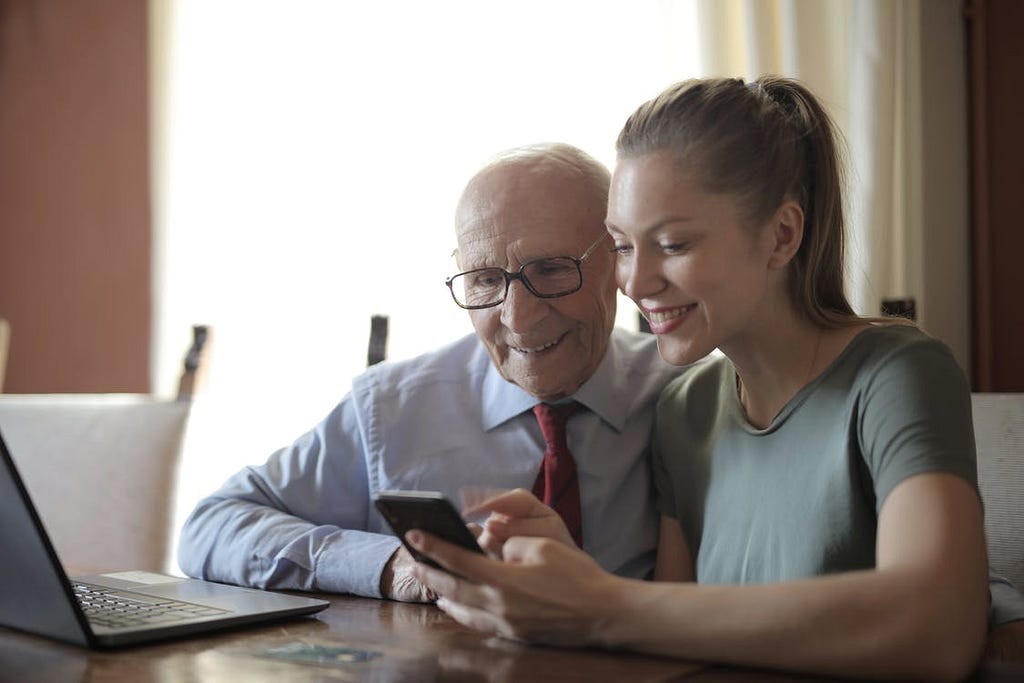 A young woman showing an elderly gentleman how to use a smartphone