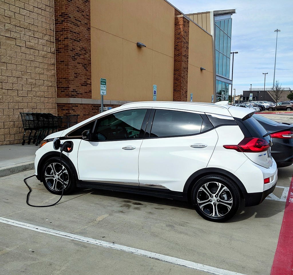 A white Chevy Bolt is being charged by an electric vehicle charger.