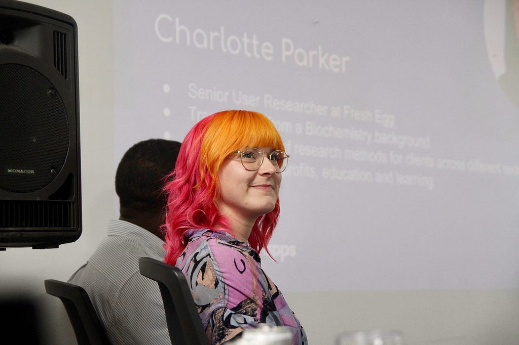 Charlotte Parker is shown next to Michael Kibedi on the panellist table with a slide showing her name and mini bio in the background