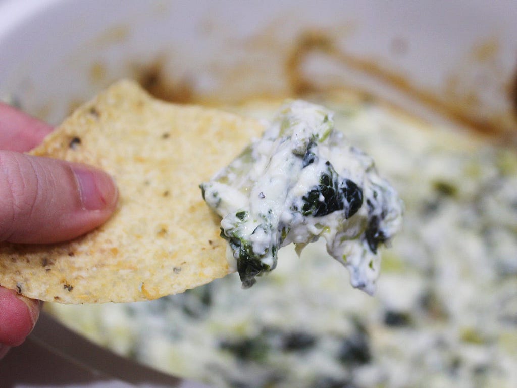 The spinach and artichoke dip on top of a tortilla chip.