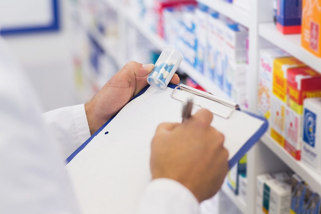Pharmacist writing on clipboard and holding medicine jar at the hospital pharmacy.