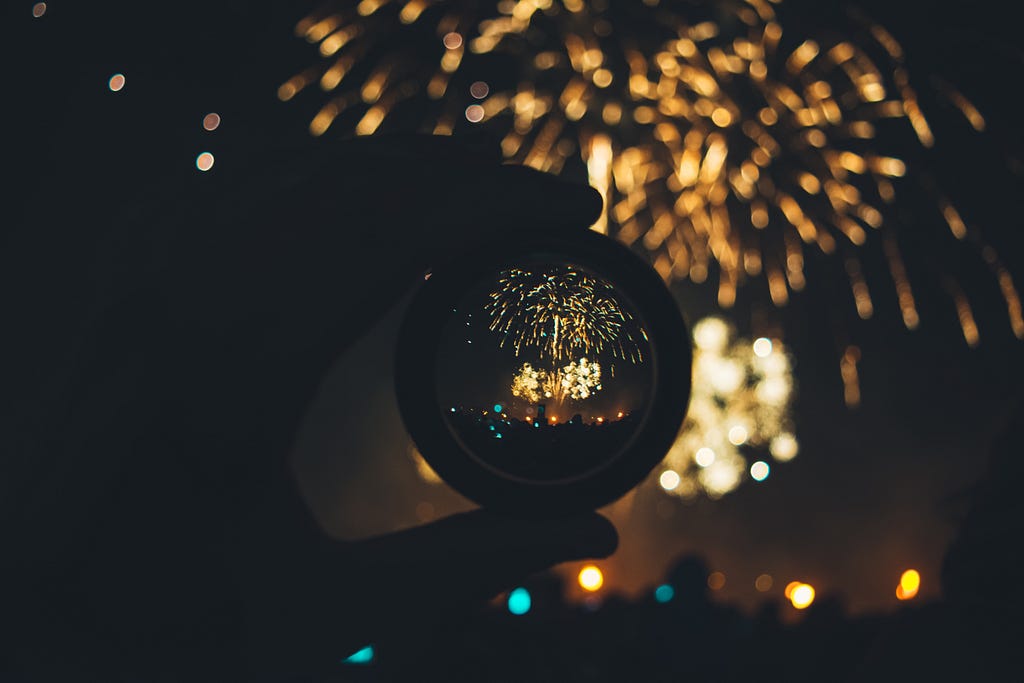 Fireworks are seen in the dark both through the camera lens held by someone and without it. Purpose inspires and pulls you.