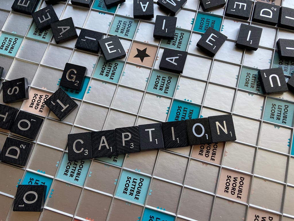 A Scrabble board covered in tiles, with “CAPTION” smelled out in tiles on the center of the board