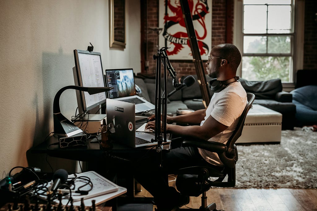 A human sitting at a desk, working on a computer, with vlogging equipment around them.