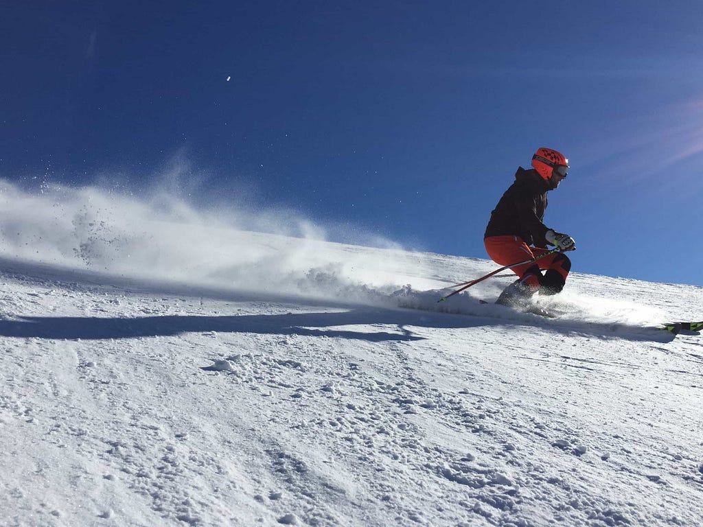 Photo of a person skiing in snow beneath a bright blue sky.