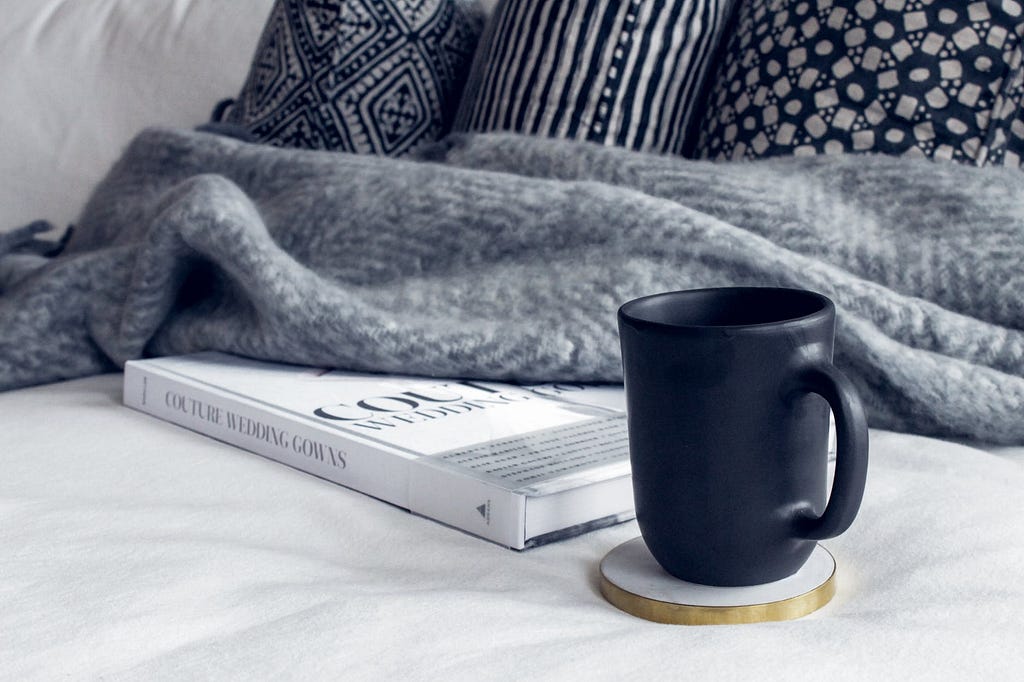 black ceramic mug on round white and beige coaster on white textile beside book