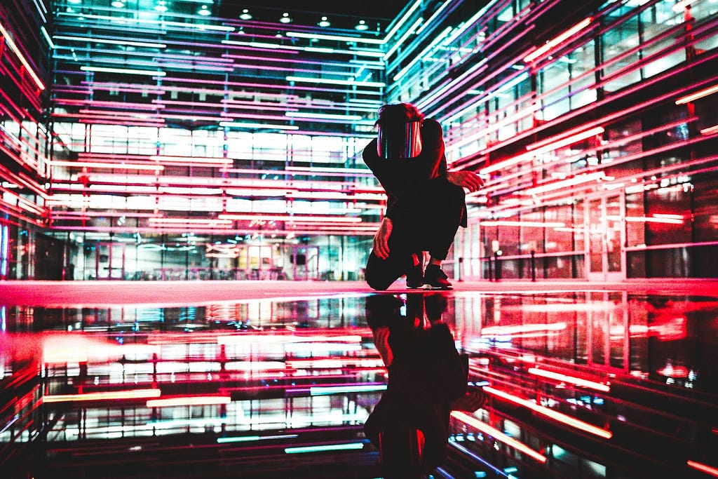 Pessoa com uma máscara agachada em meio a um ambiente urbano totalmente colorido com LEDs.