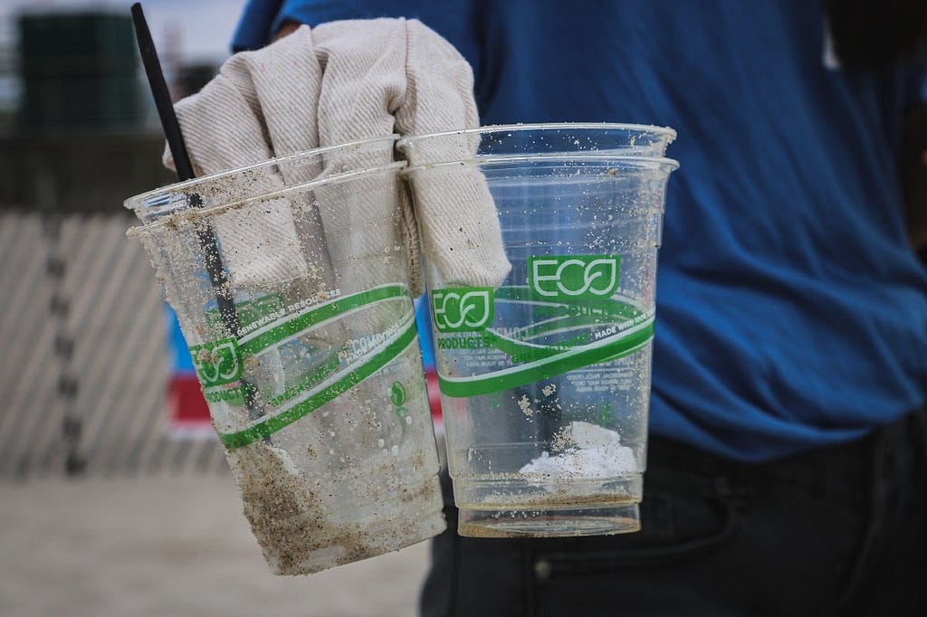 A gloved hand holds four eco labelled plastic cups that were found on the ground.