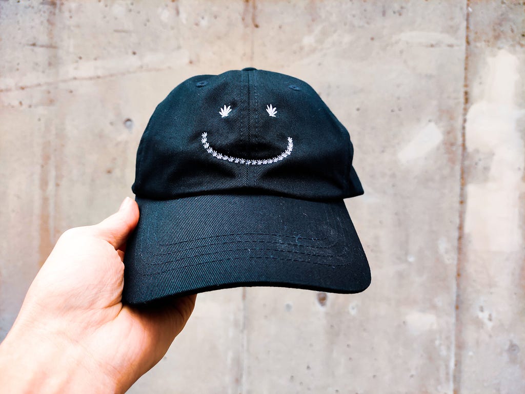 Hand holding a cap with a smile sewn on its front side