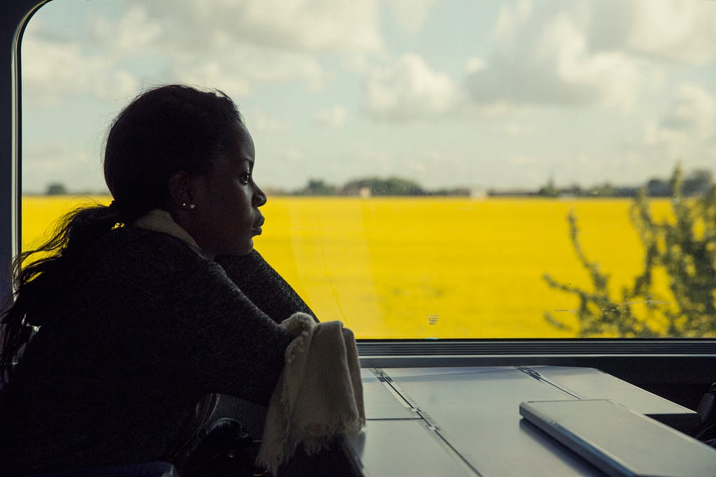 A femme presenting person staring off into the distance with a yellow field in the distance.