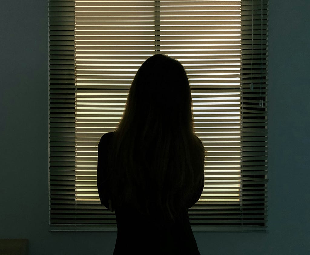 Silhouette of a woman standing in front of a window with blinds covering it