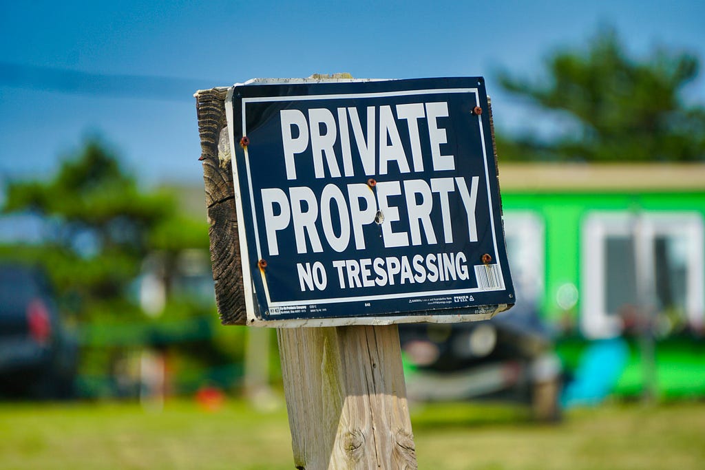 Private Property, No Trespassing sign on wooden stake, posted in front of small green house.