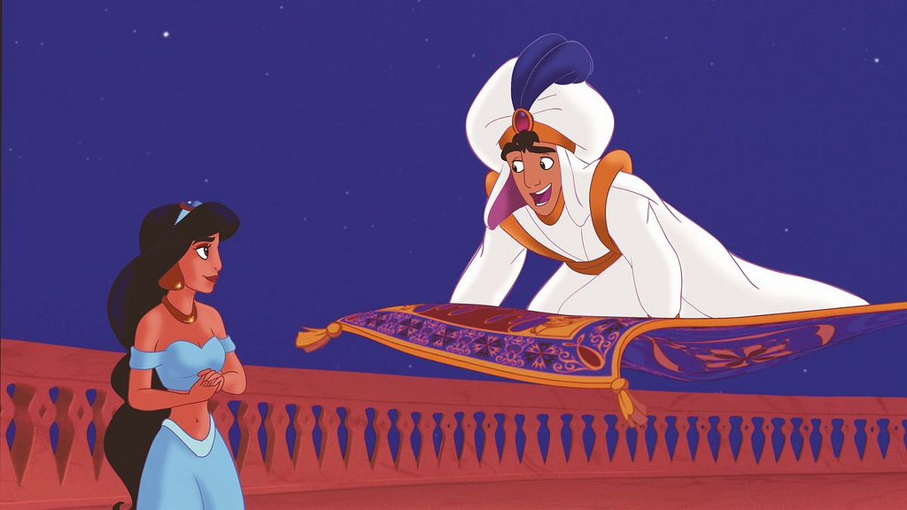 Cena do filme Aladdin, em que o personagem principal está em cima do tapete mágico, com roupas de príncipe, que são um turbante com pena, roupas brancas com mangas e calças folgadas e bufantes, com uma capa e detalhes em dourado. Ele olha para a princesa Jasmine, que usa brincos grandes e colar dourados, uma blusa curta azul, mostrando sua barriga, uma calça da mesma cor, folgada, além de uma tiara azul com dourado.
