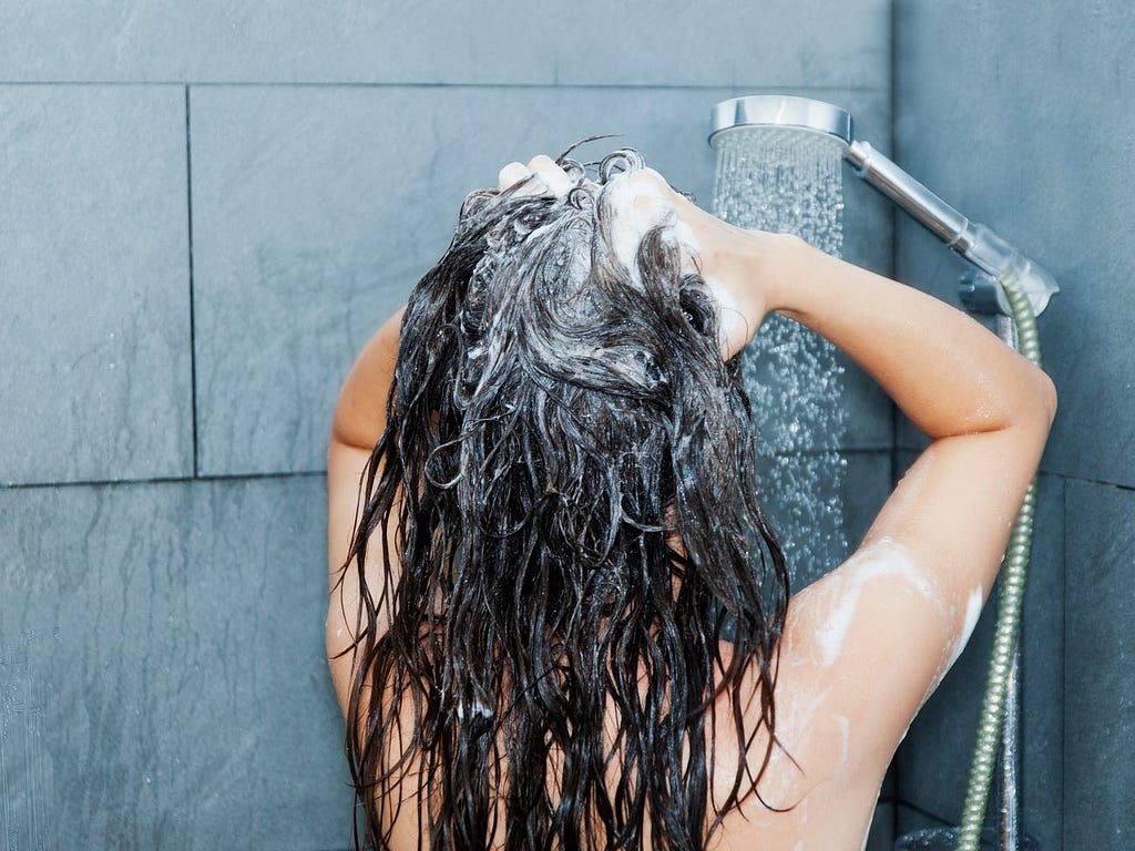 A person washes their hair in the shower.