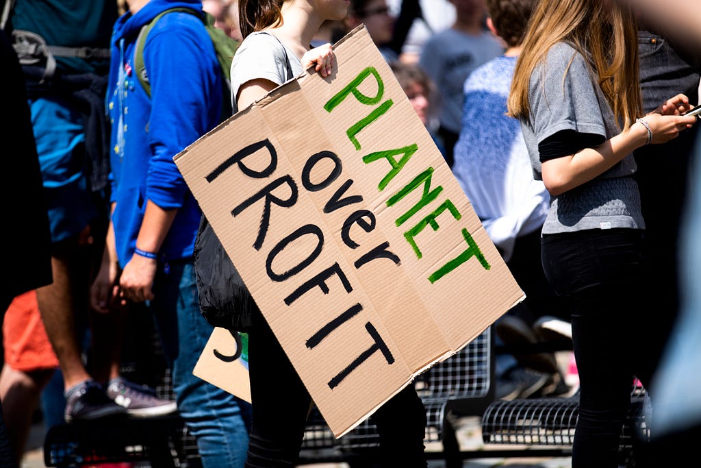 a person holding a sign that says planet over profit