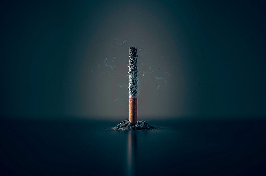A cigarette standing on its own while its been lit and its contents falling around it