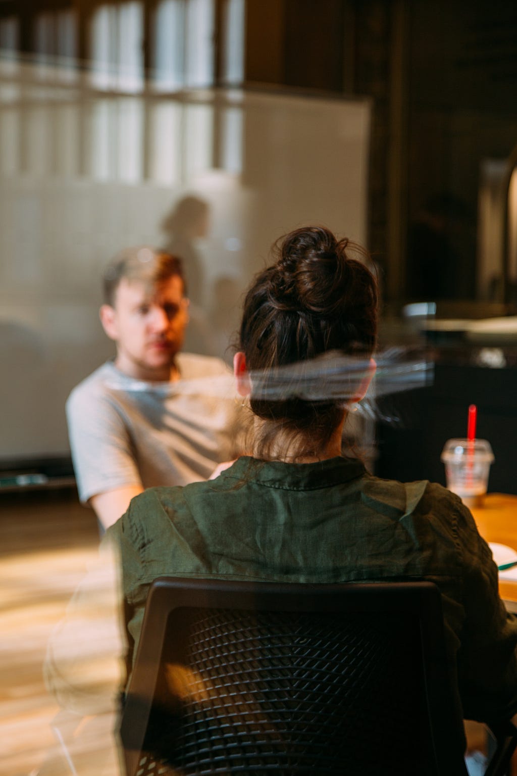 Two people in conversation, the view of the back of a female’s head, and the view of a male listening. A drink on the table. The focus is on the females head with the reader wondering what she is thinking, what assumptions is she making.