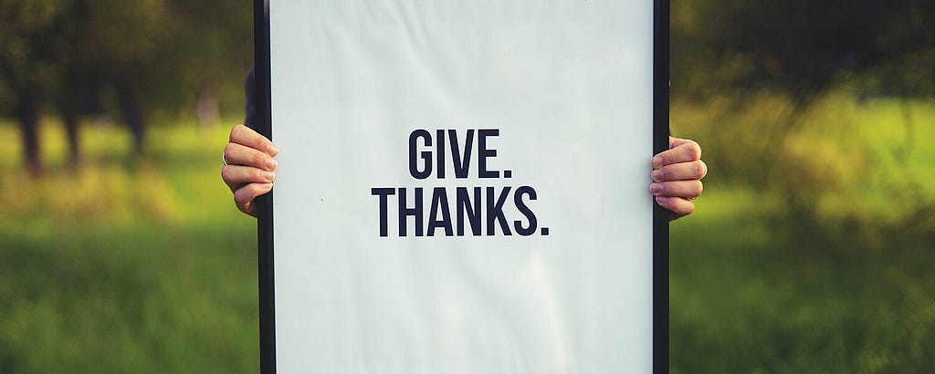 Person holding sign that says Give Thanks