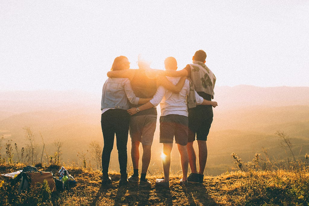 Four people huddled together, linking arms and watching the sunset.