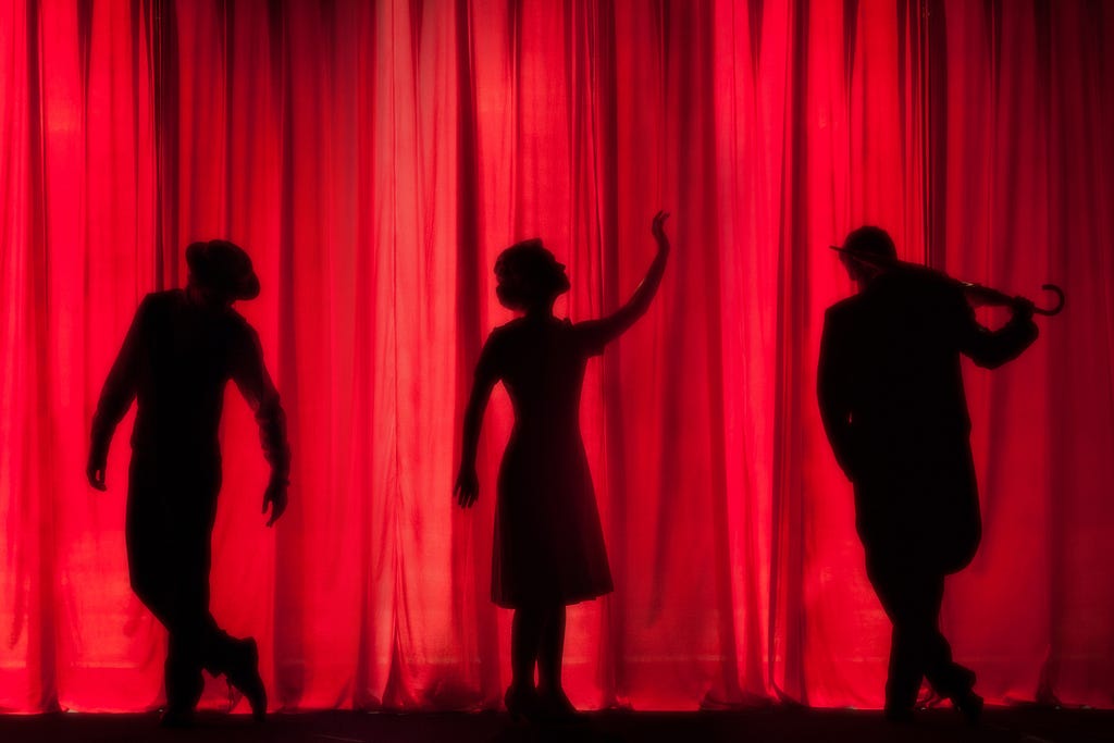 Three performers silhouetted against a red backdrop curtain