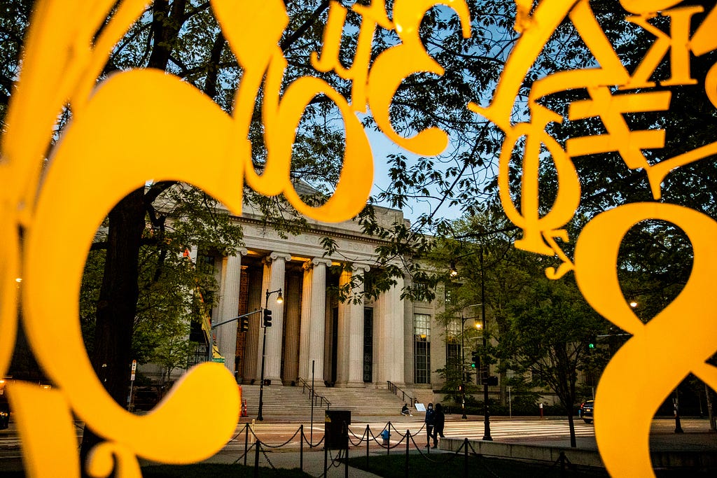 Photo of MIT building with columns. The photo was taken from the inside of a sculpture constructed of metal numbers