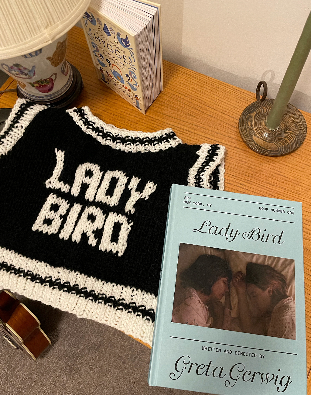 A black knitted vest with the words “Lady Bird” on it. Next to a printed version of the Lady Bird Script.