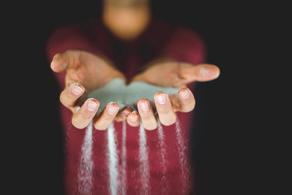 person holding sand, which is falling through their fingers