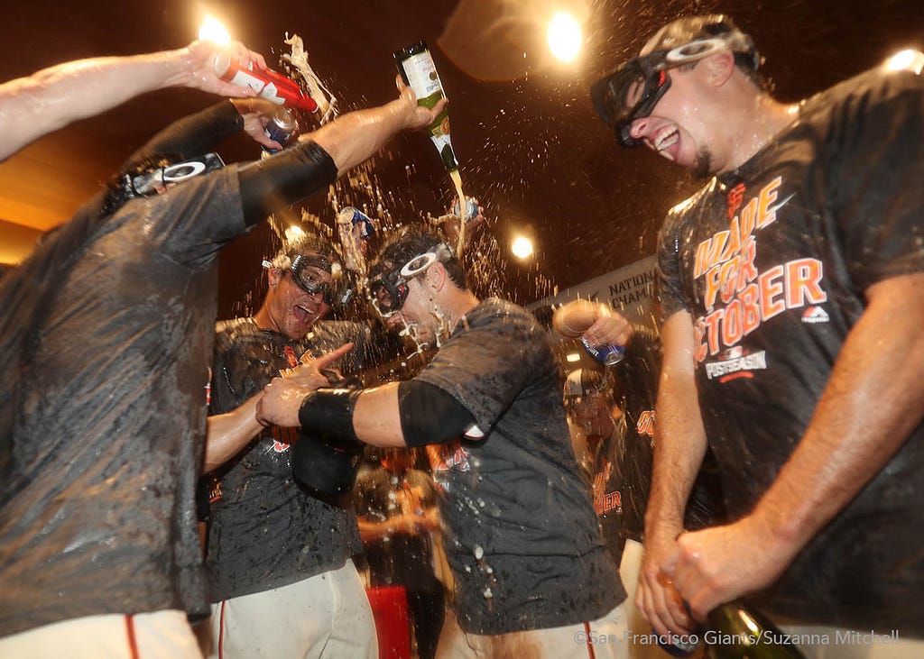 Javier Lopez, Buster Posey and Derek Law spray champagne and beer in the clubhouse.