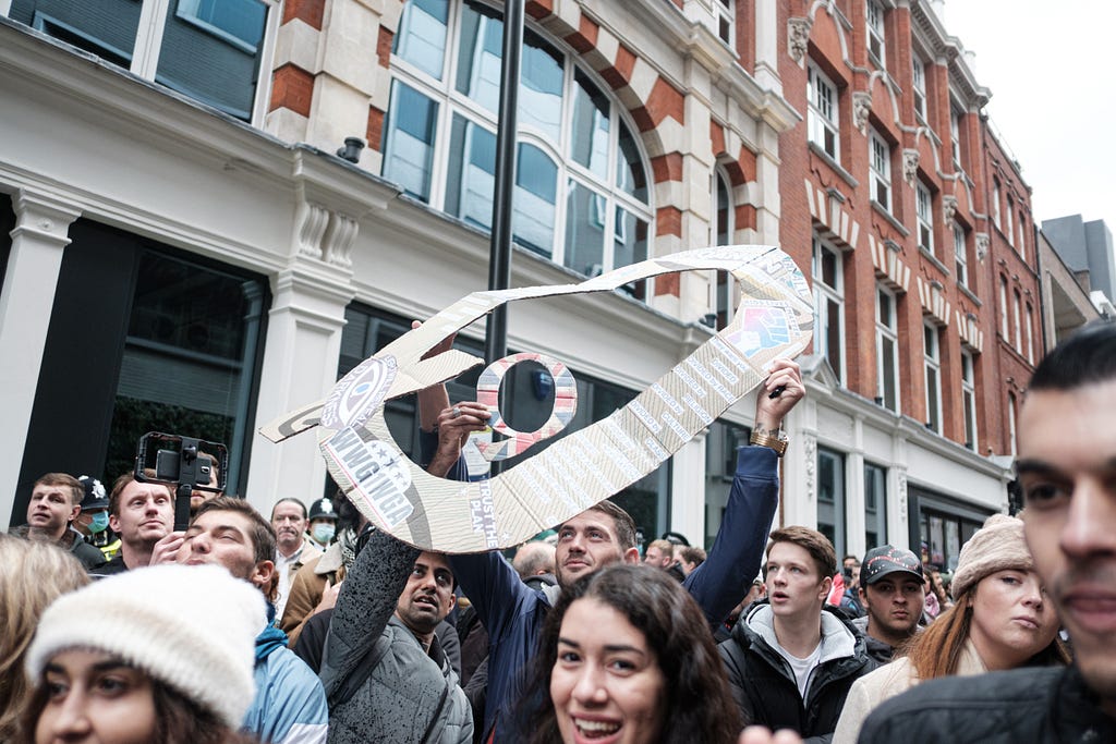 Crowd scene with demonstrator holding “Q” sign