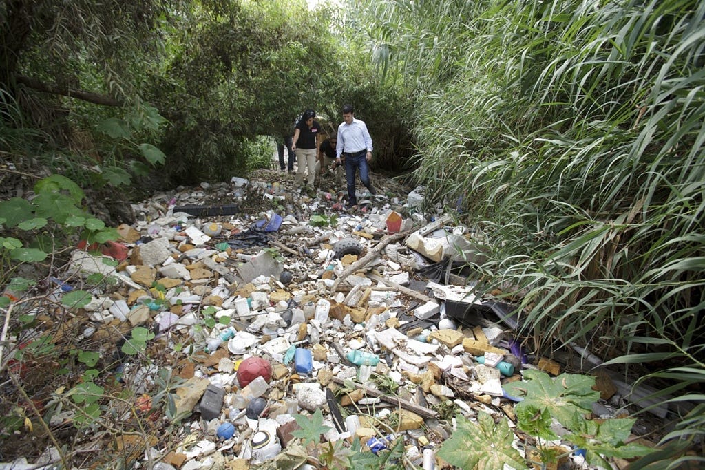 people walk through a trash-strewn river bed