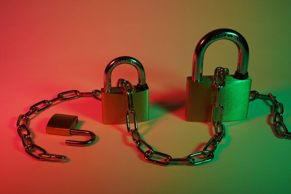 Two locked padlocks connected by a metal chain and a third unlocked padlock.