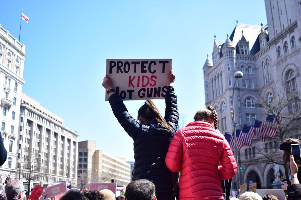 A protester holds up a sign that reads “PROTECT KIDS NOT GUNS.”