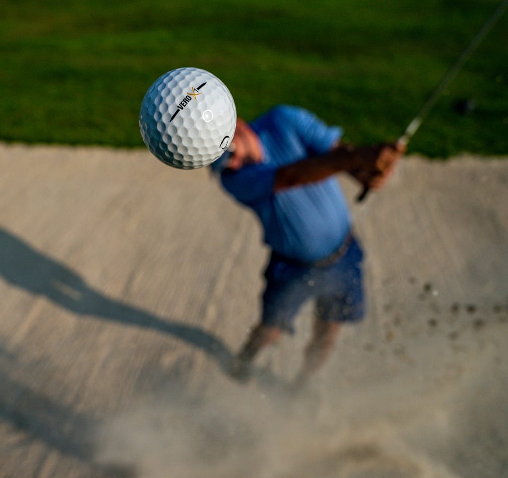 A man hitting a golf ball out of a sand bunker