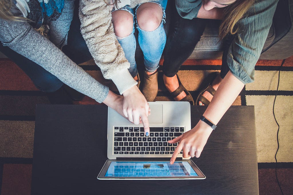 A group of people sitting by a laptop and pointing to the screen. They are collaborating.