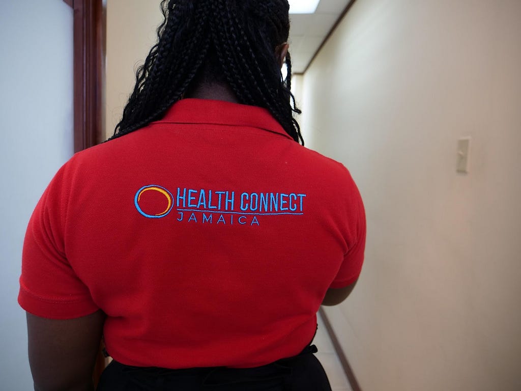 The Health Connect Jamaica logo is depicted on the back of a staff member’s shirt.