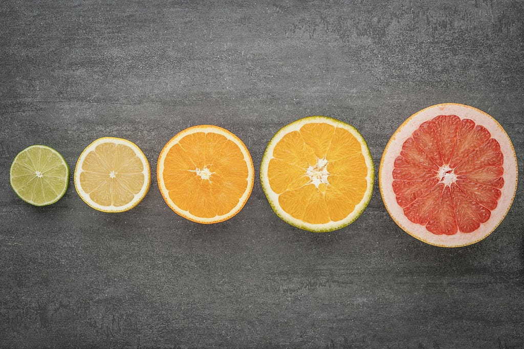 Citrus segments of various colours laying face up in a gradient of colours on a grey surface