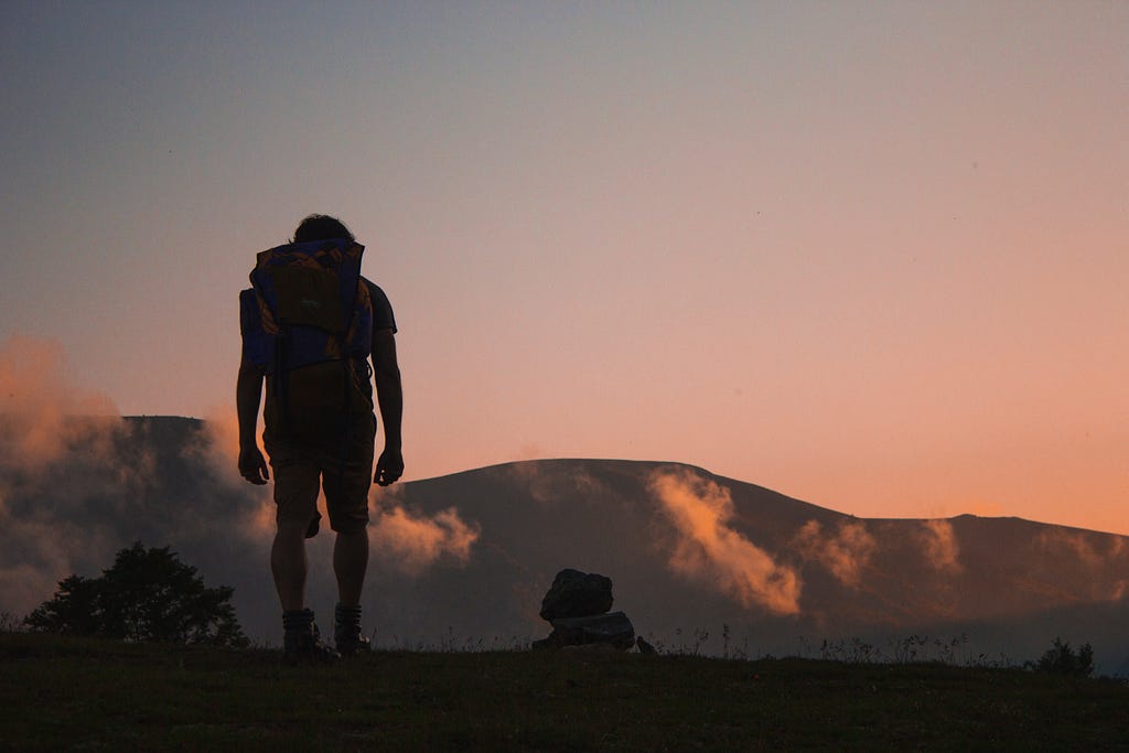 A hiker’s silhouette on top of a mountain at dusk.