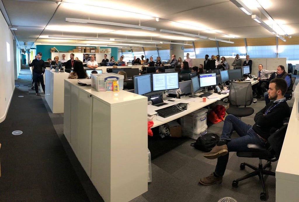 A whole team turns away from their desk to watch a show and tell presentation.