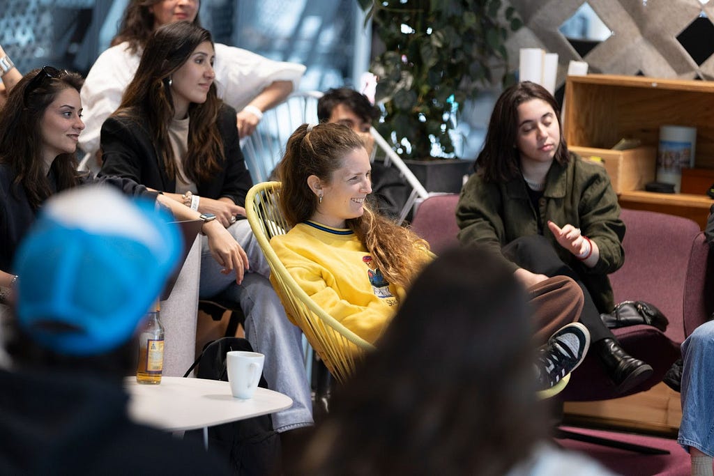 A group of students from the Elisava School of Design & Engineering, seated and listening to a discussion, with one student in focus who is wearing a bright yellow top and smiling.