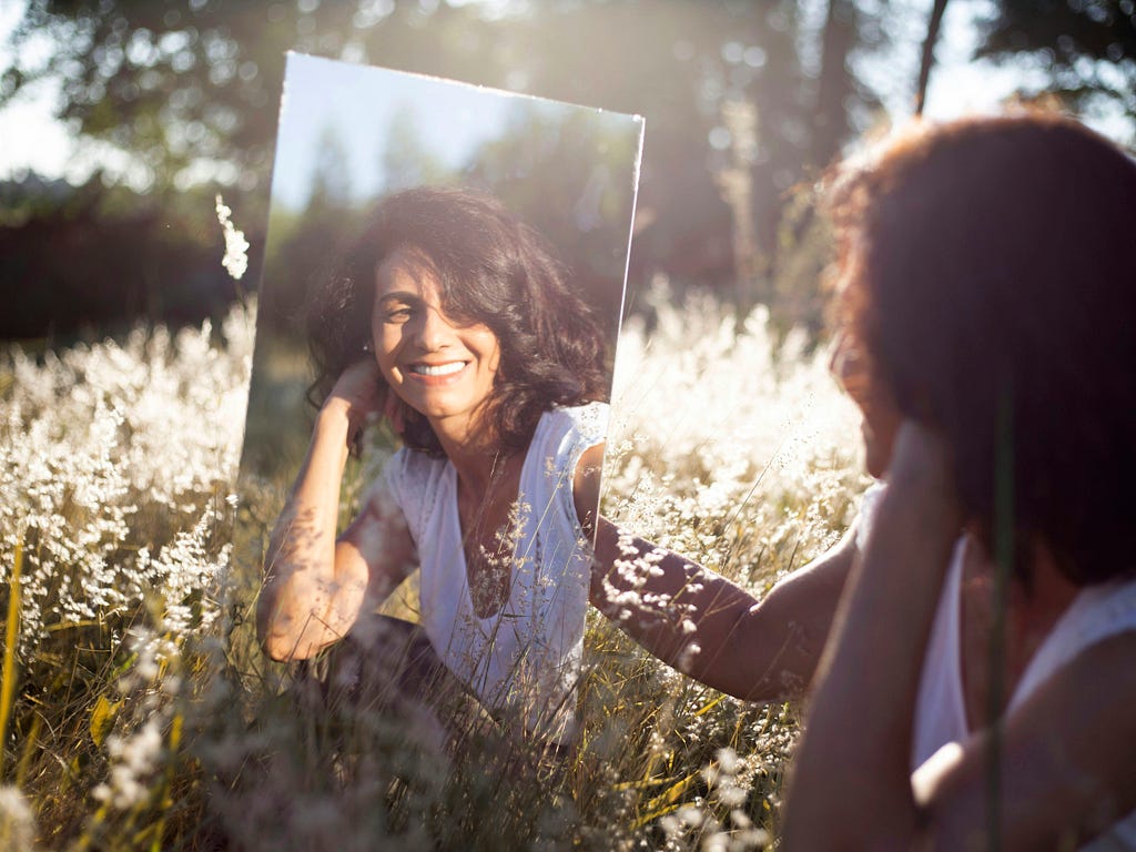 woman in field looking in mirror- New Chapter, New Me: Crafting Your Narrative After Fifty