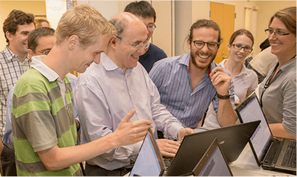 Stephen Wolfram with a smiling and laughing group of people, gathered around a screen