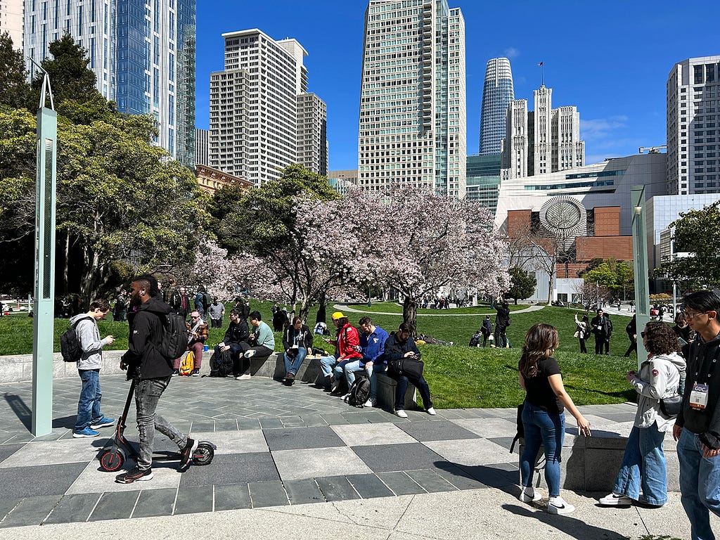 Several people milling about Yerba Buena Park in San Francisco on a bright, sunny day.